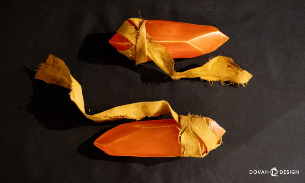 Two orange guidance soapstones, sitting on a black background, placed horizontally to the camera, with their yellow painted fabric flowing away from each stone.