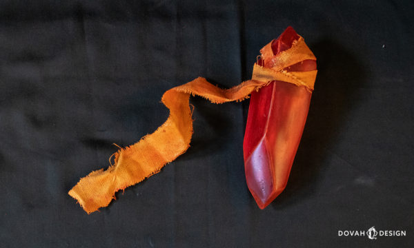 Single red sign soapstone cosplay prop, sitting on a black background, orange fabric trailing off to the left.