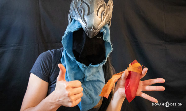 Sam of Dovah Design holding a red sign soapstone in one hand, giving a thumbs up with the other, while wearing Knight Artorias' helmet prop.