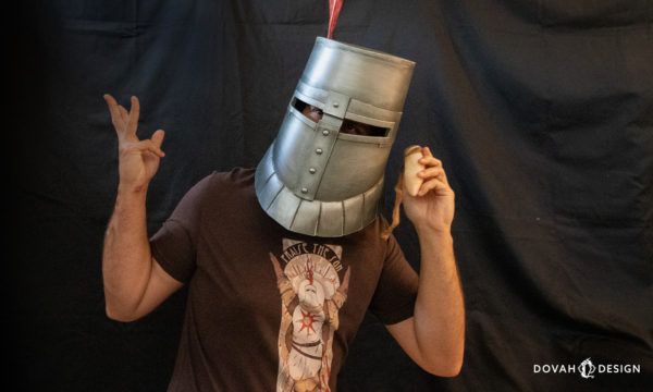 A white sign soapstone prop held by a man dressed as Solaire of Astora from Dark Souls, posing in front of a black backdrop.
