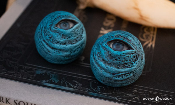 Closeup of two Blue Eye orbs sitting on a "Dark Souls" Design Works book with a White Sign Soapstone obscured but visible in the background.