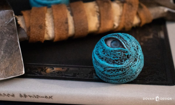 Single "Blue Eye Orb" Dark Souls prop, sitting on a Design Works book with an obscured Straight Sword hilt prop visible in the background.