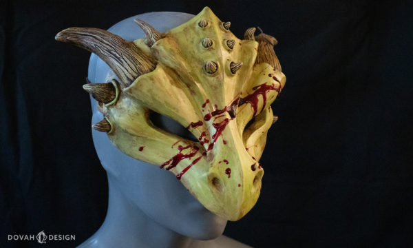 Dragon masquerade mask, in yellow-green "Zombie" style with red epoxy blood splatter, facing right on black background.