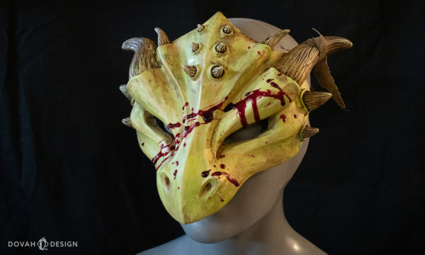 Halloween zombie dragon mask, "masquerade style," cast in yellow green urethane resin with red epoxy blood splatter, facing left on a black background.