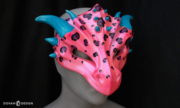 Lisa Frank inspired dragon mask, hot pink with black and purple leopard spots, teal horns, facing right on black background.