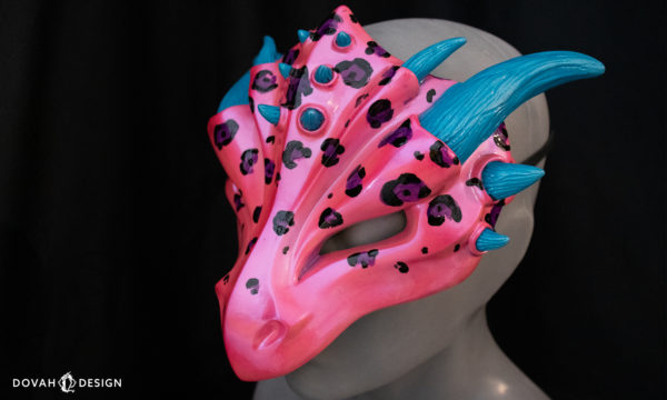 Leopard spot dragon mask, inspired by Lisa Frank, facing left on black background, showing teal horn detail.